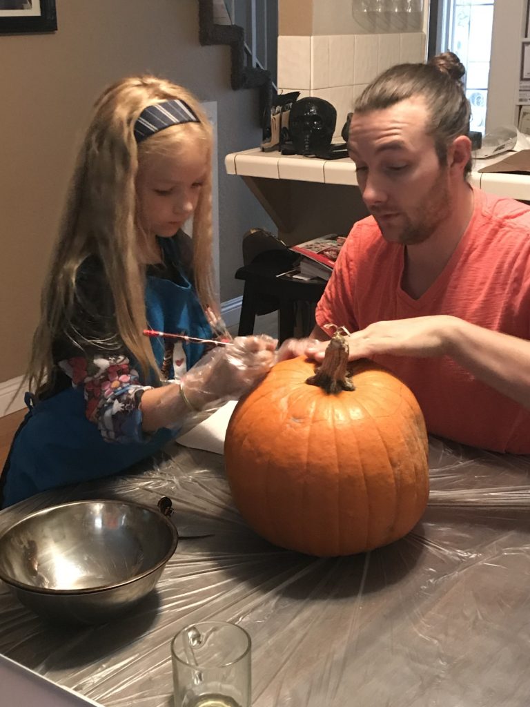 girl and dad carve pumpkin